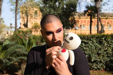 İkili olmayan ve Güney Amerika 'dan gelen genç bir insan ona iğne batıran bir bebekle vudu yapıyor. Makyaj yapıyor ve siyah elbiseler giyiyor. Kara büyü kavramı.