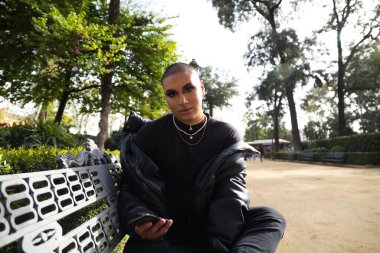 İkili olmayan ve Güney Amerikalı genç insan Avrupa 'da tatilde. Makyaj yapıyor ve siyah elbiseler giyiyor. O, parkta oturuyor ve cep telefonuna bakıyor. Eşitlik kavramı