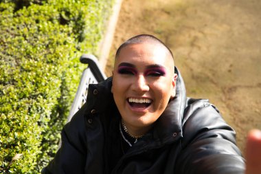 İkili olmayan ve Güney Amerikalı genç insan Avrupa 'da tatilde. Makyaj yapıyor ve siyah elbiseler giyiyor. Parkta oturmuş manken pozları veriyor. Gey güzellik ve moda konsepti.