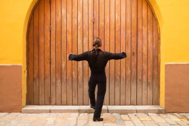 Siyah tişört ve kırmızı güllerle flamenko yapan adam ahşap bir kapının arkasında dans ederken farklı duruşlar sergiliyor. Flamenko dans konsepti insanlığın kültürel mirası. Tutkuyu hisset.