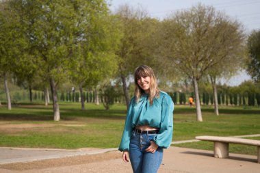 Kot pantolon ve bot giymiş güzel sarışın kadın parkta yürüyor ve Avrupa 'nın güneşli bahar gününün tadını çıkarırken fotoğrafını çekiyor. Tatil ve boş zaman kavramı.