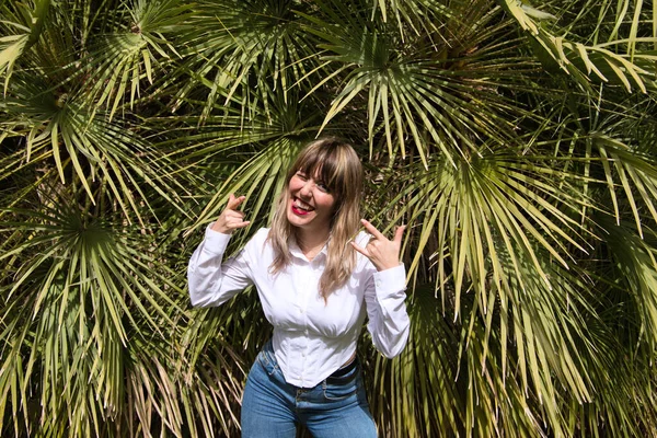 Güzel, sarışın, genç bir kadın parkta yeşil palmiye ağaçlarının önünde farklı ifadeler takınarak eğleniyor. Tatil ve boş zaman kavramı. Çeşitli ifadeler.
