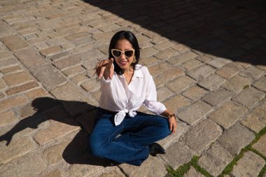 Genç, güzel, esmer, Güney Amerikalı kadın tipik bir Akdeniz şehrinde tuğla zeminde güneşleniyor. Kadın fotoğraf için poz veriyor. Tatil ve seyahat kavramı