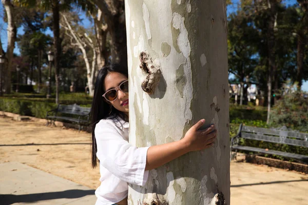 一个非常快乐的少女抱着一个巨大的树干在公园里 她的眼睛闭上了 无牙的笑着 — 图库照片