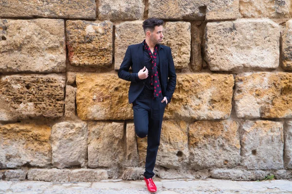 gypsy man dancing flamenco, young and handsome dressed in black and red shoes is posing and dancing on a background of a stone wall. Flamenco cultural heritage of humanity.