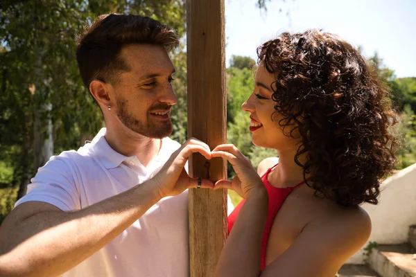 couple of latin lovers leaning on a wooden poster forming a heart with their hands. The man is camouflaging the woman to make her fall in love. They are bachata dancers. Latin dance concept.