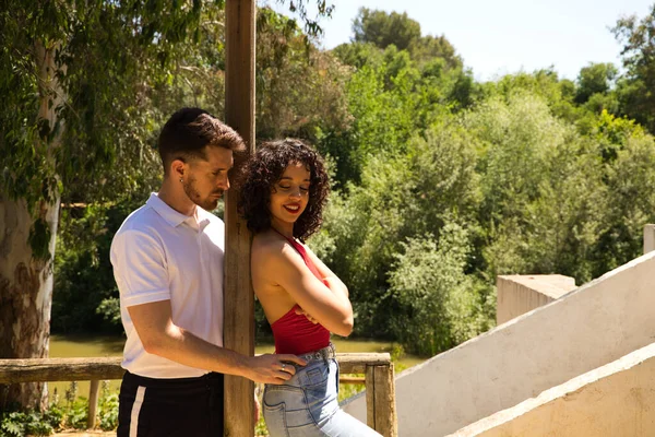 Latin lovers couple leaning on a wooden poster in a sensual way. The man is camouflaging the woman to make her fall in love. They are bachata dancers. Latin dance concept.