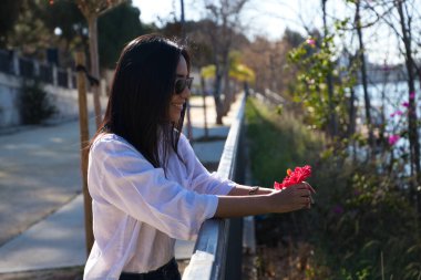 Güney Amerika 'dan genç ve güzel bir kadın Avrupa turnesinde. Kadın elinde kırmızı bir çiçek tutuyor ve Seville 'deki nehrin kenarındaki korkuluklara yaslanıyor. Seyahat ve turizm kavramı.