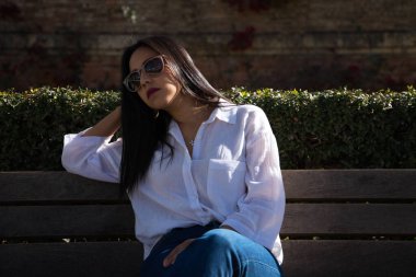 Genç, güzel, esmer, Güney Amerikalı kadın bir bankta dalgın ve üzgün oturuyor, ayrıca depresyonda ve endişeli. Farklı ifadeleri kavra.