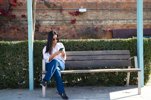 年轻美丽的南美女子在欧洲观光 这个女人正坐在一张木制长椅上检查她的社交网络和电子邮件 旅行和旅游概念 — 图库照片