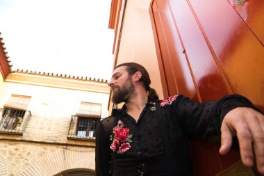 Kırmızı ahşap bir kapının arkasında siyah tişört ve kırmızı güllerle flamenko yapan bir adam, kapıya yaslanarak bekliyor. Flamenko dans konsepti insanlığın kültürel mirası.