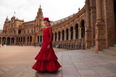 Beautiful teenage woman dancing flamenco in a square in Seville, Spain. She wears a red dress with ruffles and dances flamenco with a lot of art. Flamenco cultural heritage of humanity.