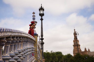 Sevilla 'nın ünlü meydanına bakan bir köprüde flamenko yapan güzel bir genç kadın kırmızı bir elbise giyiyor ve kafasında kırmızı çiçekler var. İnsanlığın Flamenko kültürel mirası