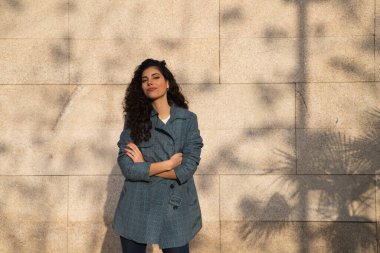 Kahverengi saçlı, kıvırcık burunlu, şık elbiseli güzel bir genç kadın kahverengi arka planda bir süper model olarak poz veriyor. Güzellik ve moda kavramı.