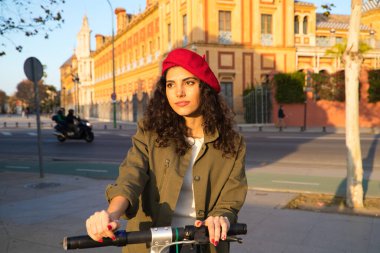 Kıvırcık kahverengi saçlı, kırmızı şapkalı ve günlük kıyafetler giyen güzel Latin bir kadın Avrupa 'da motosikletle şehri geziyor. Turizm konsepti.