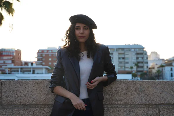 Kıvırcık kahverengi saçlı, siyah şapkalı, sıradan kıyafetler giymiş ve Sevilla 'yı gezen güzel bir genç kadının portresi. Arka planda güneş var. Turizm konsepti.