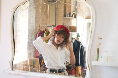 Genç, güzel, girişken bir kadın. Resim ve moda tasarımı sanatına adanmış, kafasına kırmızı bir bere takıyor ve stüdyosunun aynasında kendine bakıyor. Girişimci kadın..