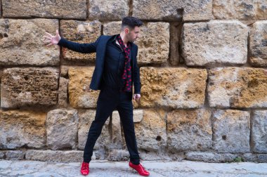 Çingene adam flamenko yapıyor, siyah ve kırmızı ayakkabılar giymiş genç ve yakışıklı taş bir duvarın arkasında poz veriyor ve dans ediyor. İnsanlığın Flamenko kültürel mirası.