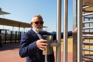 Olgun, gri saçlı, sakallı, ceketli ve kravatlı bir adam iş adamı ve yönetici olarak çalıştığı binaya giriyor. Binaya girmek için parmak iziyle kapıyı açıyor..