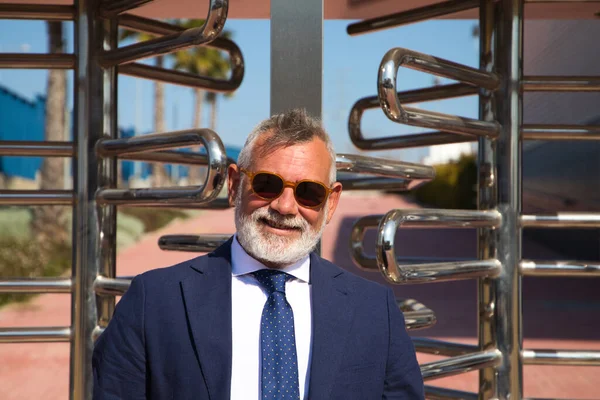 Handsome, mature, grey-haired man with beard, jacket and tie and sunglasses is on the university campus where he works as a university lecturer. Concept professor, university rector.