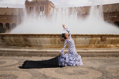 Dişi flamenko dansçısı, genç esmer ve güzel tipik İspanyol dansçı Seville Meydanı 'ndaki bir fıskiyenin önünde siyah bir şalla dans ediyor. Flamenko dünya kültür mirası konsepti.