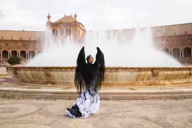 Dişi flamenko dansçısı, genç esmer ve güzel tipik İspanyol dansçı Seville Meydanı 'ndaki bir fıskiyenin önünde siyah bir şalla dans ediyor. Flamenko dünya kültür mirası konsepti.