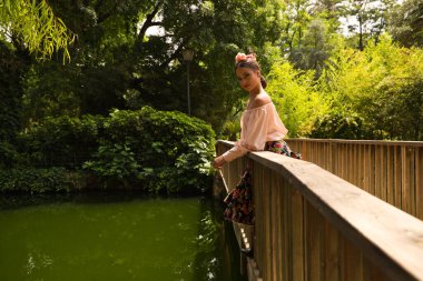 Çiçekli bir etek giymiş, saçı fırfırlı ve çiçekli güzel bir flamenko dansçısı. Tahta bir köprüden eğiliyor. Flamenko kavramı insanlığın kültürel mirası.