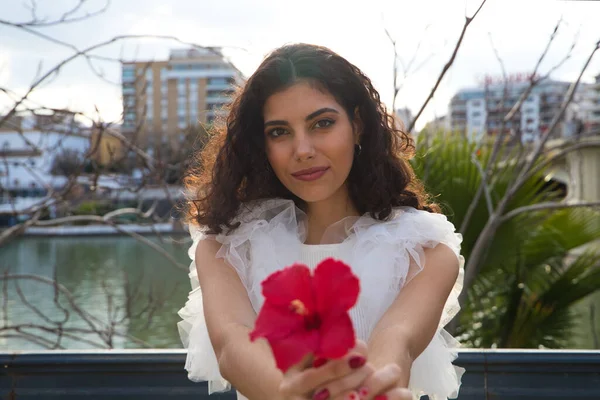 Genç, güzel, siyah, kıvırcık saçlı ve burnu kalkık bir kadın. Kadın fotoğraf için egzotik kırmızı bir çiçekle poz veriyor. Nehir arka planda görülebilir. Güzellik ve moda konsepti.