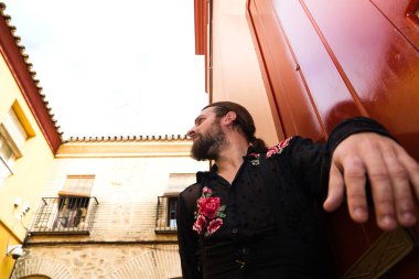 Kırmızı ahşap bir kapının arkasında siyah tişört ve kırmızı güllerle flamenko yapan bir adam, kapıya yaslanarak bekliyor. Flamenko dans konsepti insanlığın kültürel mirası.