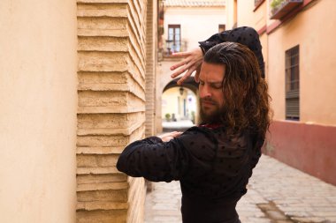 Siyah gömlek ve kırmızı güllerle flamenko dansı yapan uzun saçlı adam. Sevilla 'nın tipik dar bir sokağında elleriyle dans ediyor. Flamenko dans konsepti insanlığın kültürel mirası.