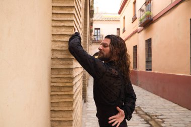 Siyah gömlek ve kırmızı güllerle flamenko dansı yapan uzun saçlı adam. Sevilla 'nın tipik dar bir sokağında elleriyle dans ediyor. Flamenko dans konsepti insanlığın kültürel mirası.