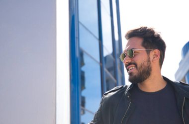 Sakallı, heykel vücutlu ve güneş gözlüklü genç ve yakışıklı bir adam cam bir binada çalıştığı ofisten ayrılıyor. Kavram yönetimi, yönetim, ofis, şirket, patron.