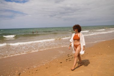 Sahilde yürüyen bikinili güzel bir kadın. Kadın farklı jestler ve ifadeler yaparken bir cennet kumsalına yolculuğunun tadını çıkarıyor..