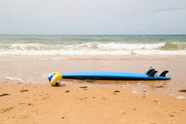 Surfboard and volleyball on the sand of the beach on the shore. In the background you can see the sea. Concept outdoor sports.