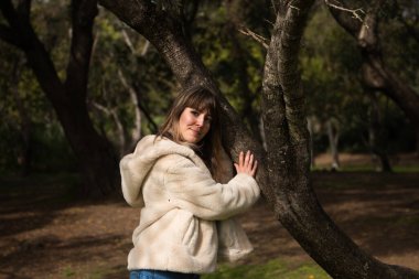 Kot pantolon giymiş, beyaz şapkalı ve botlu genç ve güzel sarışın kadın parkta yürüyor ve ağaçların arasında güneşli bir günün tadını çıkarırken fotoğrafını çekiyor. Boş zaman kavramı.