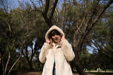 Kot pantolon giymiş, beyaz şapkalı ve botlu genç ve güzel sarışın kadın parkta yürüyor ve ağaçların arasında güneşli bir günün tadını çıkarırken fotoğrafını çekiyor. Boş zaman kavramı.