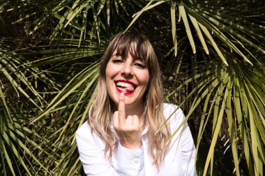 Güzel, sarışın, genç bir kadın parkta yeşil palmiye ağaçlarının önünde farklı ifadeler takınarak eğleniyor. Tatil ve boş zaman kavramı. Çeşitli ifadeler.