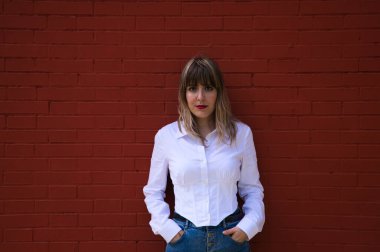 Güzel, sarışın, genç bir kadın kırmızı arka plan duvarının önünde farklı ifadeler kullanırken eğleniyor. Çeşitli ifadeleri kavra. Kahkaha, üzüntü, yorgun, kızgın, nefret.