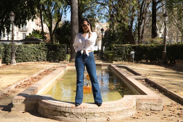 Genç, güzel, esmer bir kadın Seville 'deki bir fıskiyenin kenarında. Güney Amerikalı kadın Avrupa 'da turizm yapıyor ve tatilinin tadını çıkarıyor..