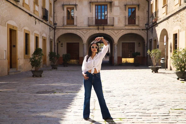 Genç, güzel ve esmer Güney Amerikalı kadın, Akdeniz şehrinin tipik sütunları ve kemerleriyle Seville meydanını geziyor. Kadın fotoğraf için poz veriyor. seyahat kavramı