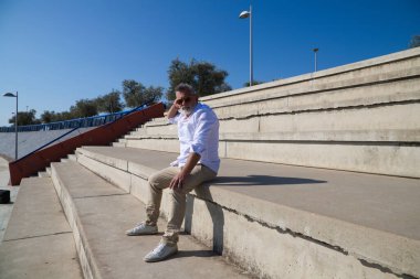 Sakallı ve gri saçlı yakışıklı olgun bir adam açık hava konferans salonunun merdivenlerinde oturuyor. Adam farklı yerlere bakıyor. Kıdemli konsept, seyahat ve turizm.