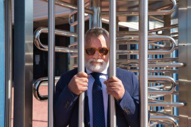 Olgun, gri saçlı, sakallı, güneş gözlüklü, işyeri çitlerinin arkasında. İş yerinde stres ve baskı kavramı, depresyon, acı, iş yerinde taciz.