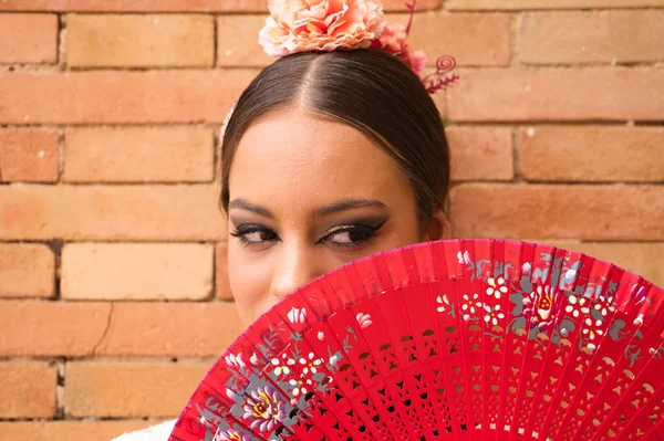 Beautiful teenage flamenco dancer with brunette hair and dressed in dance clothes makes different postures and expressions with a red fan while covering her face. Language of the fan.