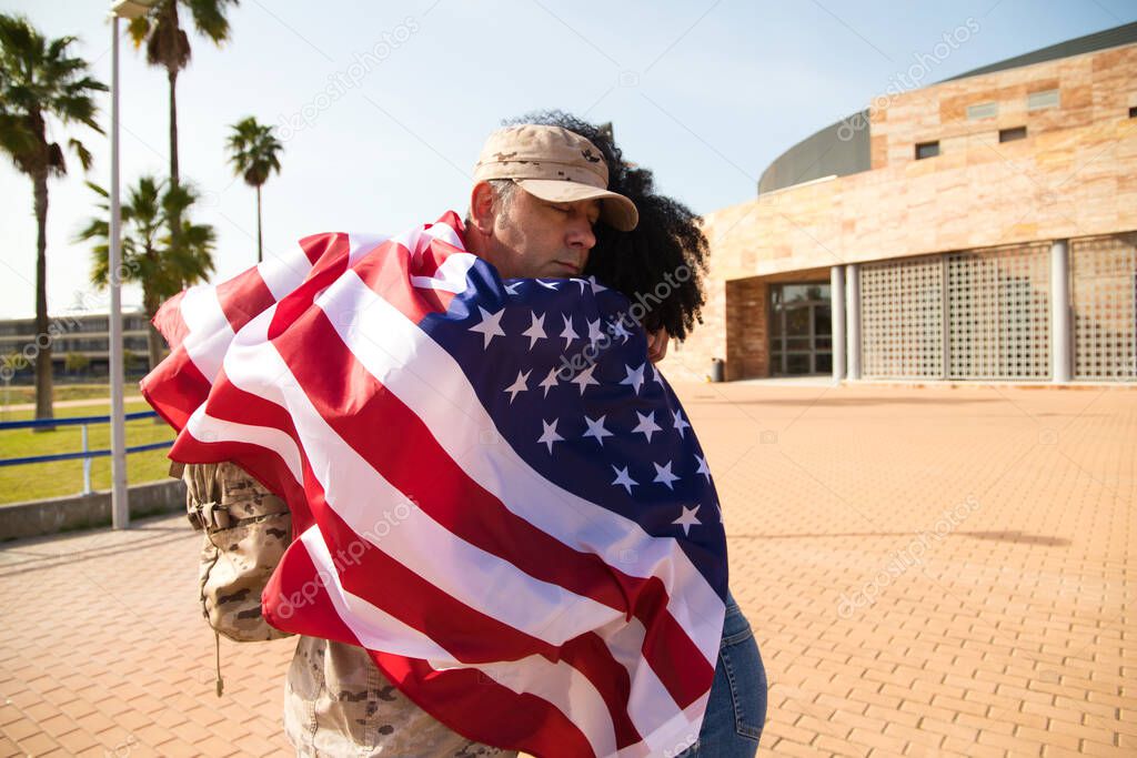 A beautiful African-American woman and an American soldier embrace wrapped in the American flag. The soldier has returned from war and special missions. Concept of war and army.