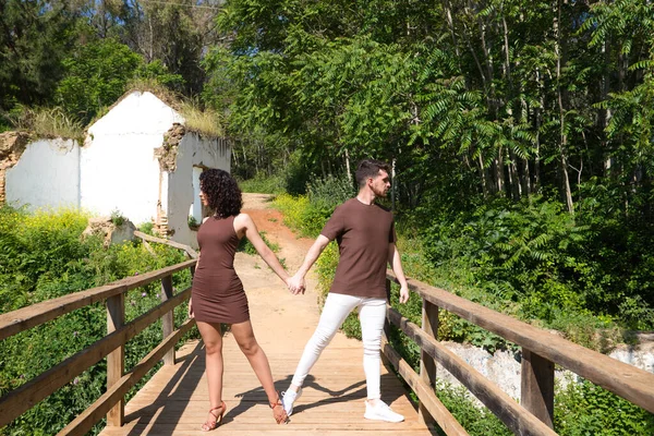 Young and handsome latin dance couple salsa and bachata in the park on a wooden bridge. The couple dances passionately and in love surrounded by greenery and trees. Dance concept.