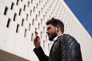 Sakallı, heykel gibi vücudu olan yakışıklı genç adam sokakta yürürken güneş gözlüğünü çıkarıyor ya da takıyor. Turizm ve şehir yürüyüşleri kavramı