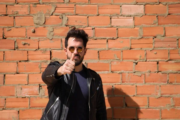 Genç, esmer, sakallı, vücudu yontulmuş Latin bir adam elleriyle mükemmel bir baş parmak işareti yapıyor. Arka planda kırmızı tuğla duvar var. Anlaşma kavramı, doğru, mükemmel, iyi.