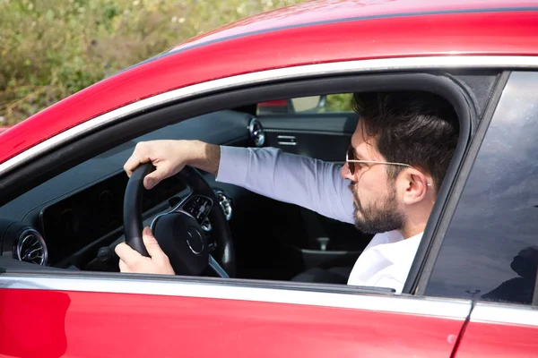 Young handsome man, sculpted body sitting in his red sports car. The man is wealthy and dressed in modern clothes. High standard of living and well positioned financially.
