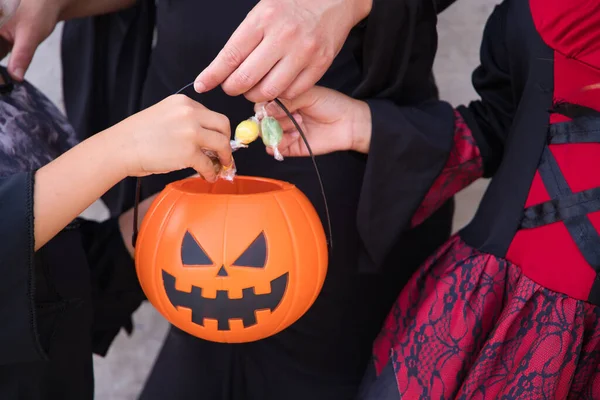 Happy halloween. Details of hands of woman, boy and girl putting candy and sweets in a Halloween pumpkin. Trick or treat.