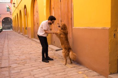 handsome, young Hispanic man with his brown golden retriever dog, holding hands while looking at each other. Concept pets, animals, dogs, pet love, golden retriever.